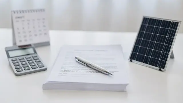 Vertrag zum Photovoltaik-Widerruf mit Kalender, Stift und Solarmodell auf hellem Schreibtisch